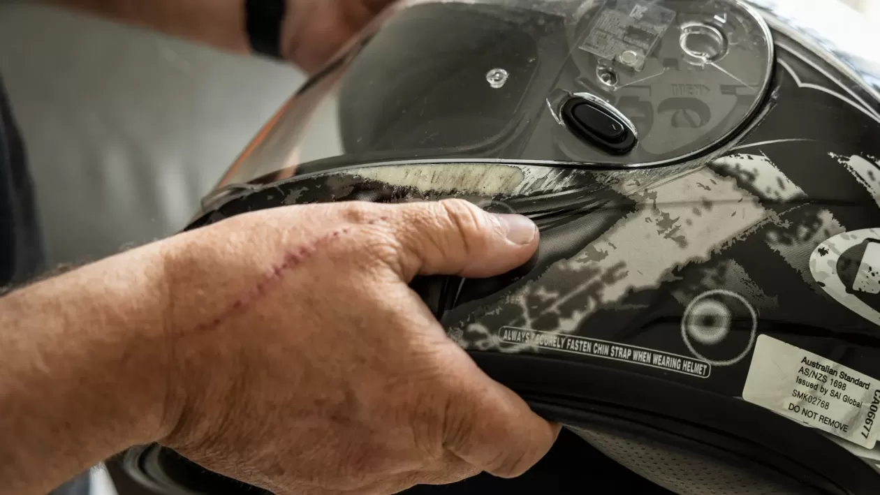 A person holds a helmet which shows scratches after being damaged in a crash.