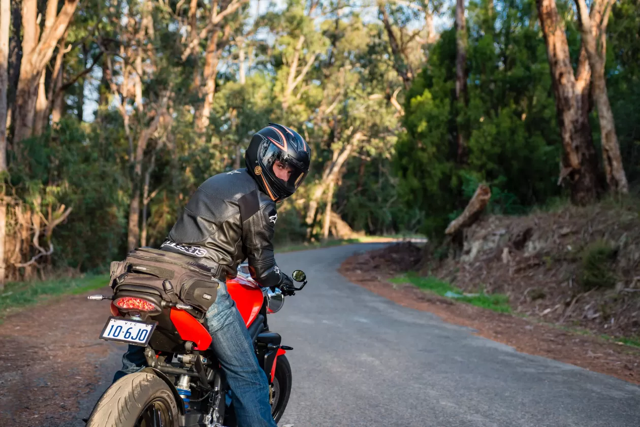 A man riding a red motorcycle on a road in the bush
